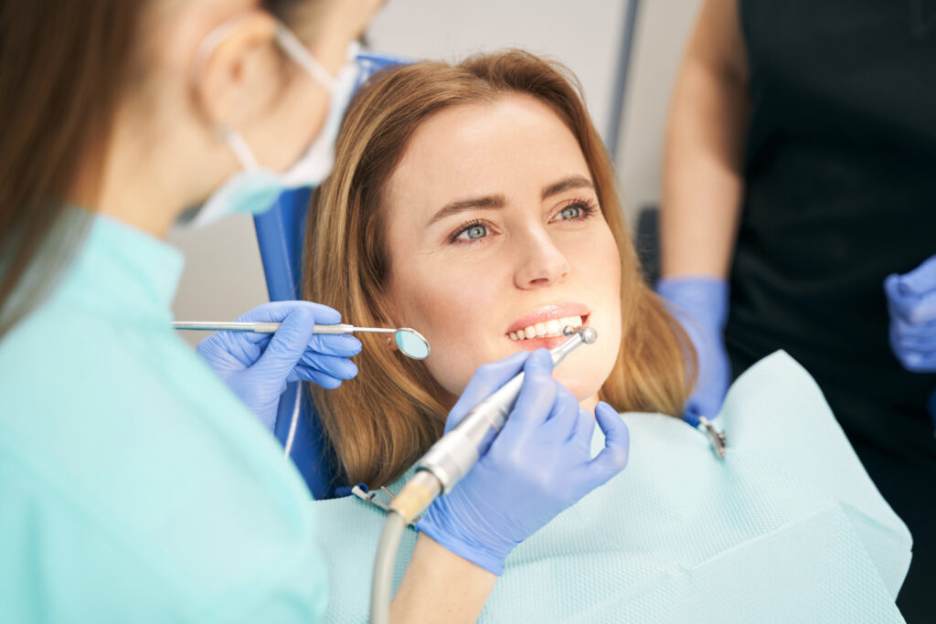 Female doctor in sterile gloves using dental mirror and dental care equipment while doing teeth treatment in stomatology clinic