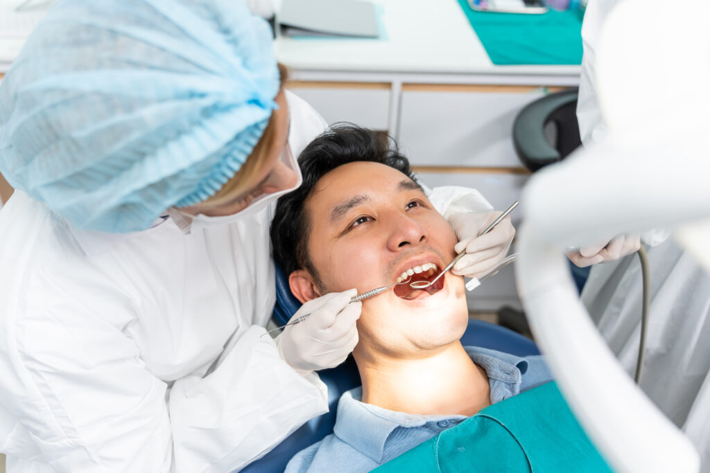 Caucasian dentist examine tooth for young man patient at dental clinic. Attractive male lying on dental chair, get dental treatment from female doctor during procedure appointment service in hospital.