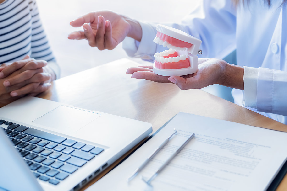 Dentist showing and explaining teeth disease treatment to patient using teeth model denture and explorer mirror tool in dental clinic office. Healthcare concept.