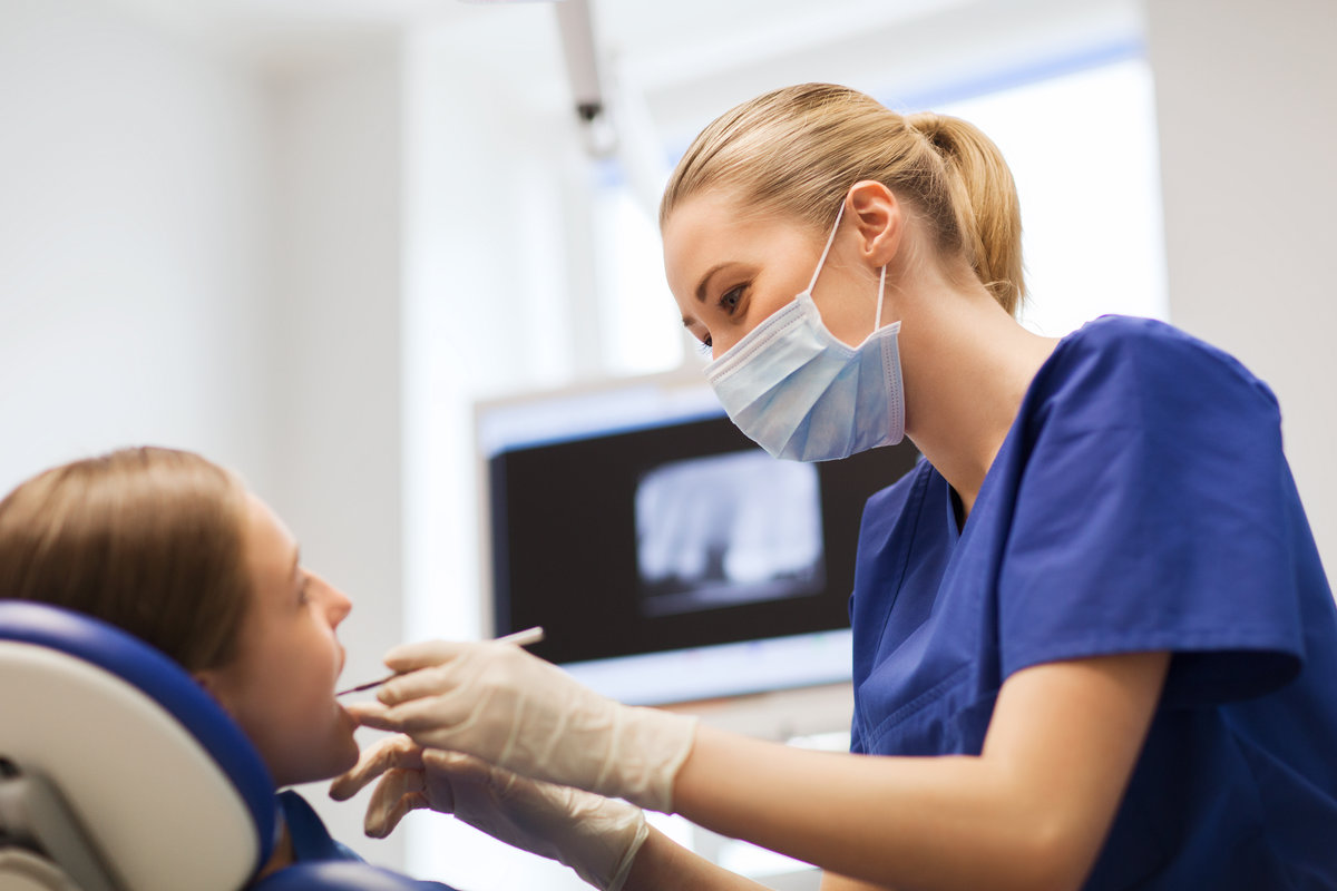 people, medicine, stomatology and health care concept - happy female dentist with mirror or dental probe checking patient girl teeth up at dental clinic office